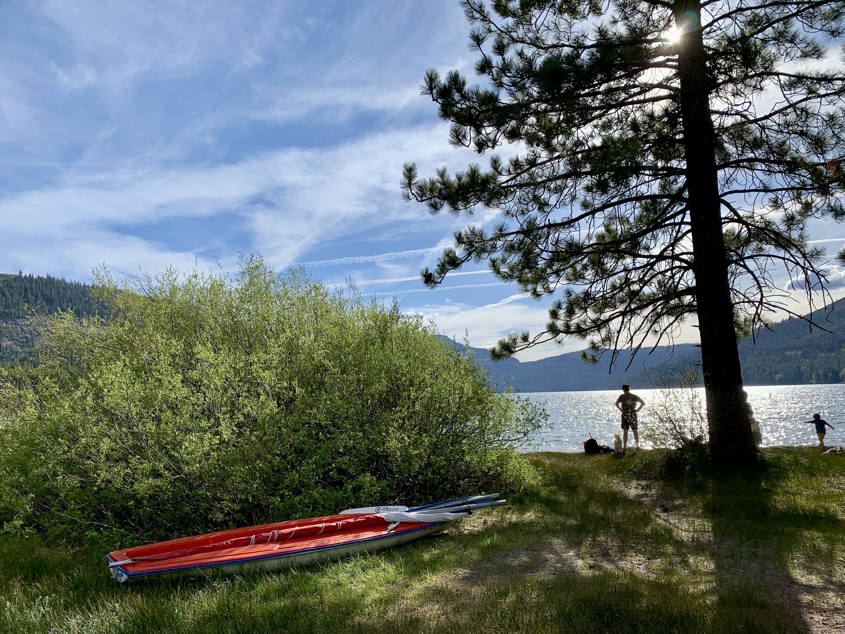 A family and dog on the grassy summer shoreline of Donner Lake with a kayak